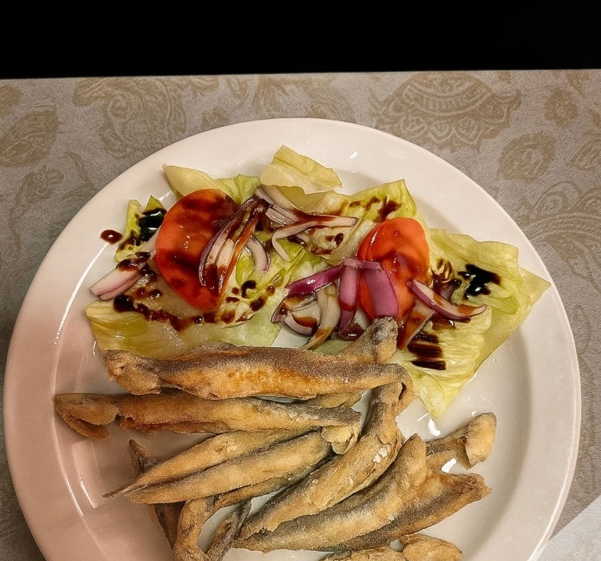Pescaditos fritos servidos con ensalada de lechuga, tomate y cebolla